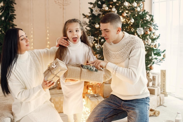 Junge Familie, die nahe Weihnachtsbaum sitzt und zusammen feiert