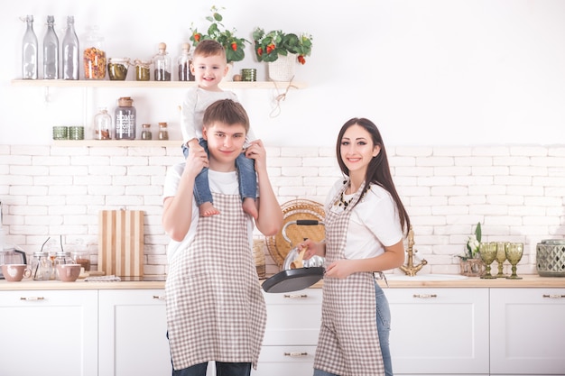 Junge Familie, die zusammen kocht. Ehemann, Ehefrau und ihr kleines Baby in der Küche. Familie, die den Teig mit Mehl knetet. Die Leute kochen das Abendessen oder Frühstück.