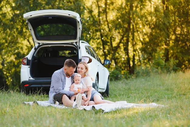 Junge Familie drei Leute in weißen Kleidern haben Picknick. Schöne Eltern und Tochter reisen in den Sommerferien mit dem Auto.