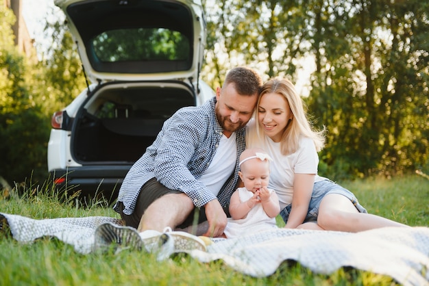 Junge Familie drei Leute in weißen Kleidern haben Picknick. Schöne Eltern und Tochter reisen in den Sommerferien mit dem Auto.