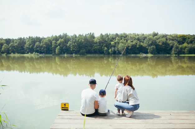 Junge Familie, Frau, Mann und zwei kleine Kinder, die am See angeln, Mann und Frau verbringen ein schönes Wochenende zusammen