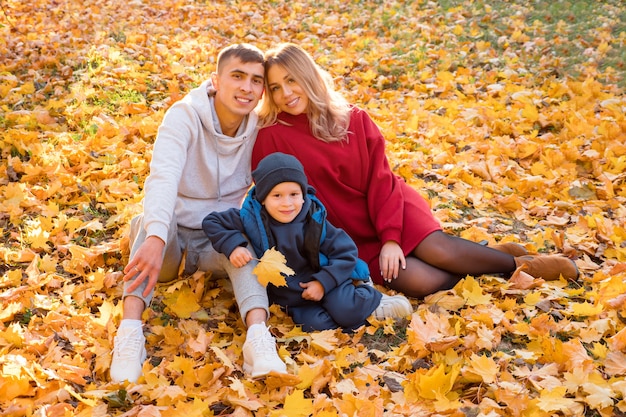 Junge Familie für einen Spaziergang. Mann, Frau, Kind sitzen an einem warmen Herbsttag auf dem Boden.