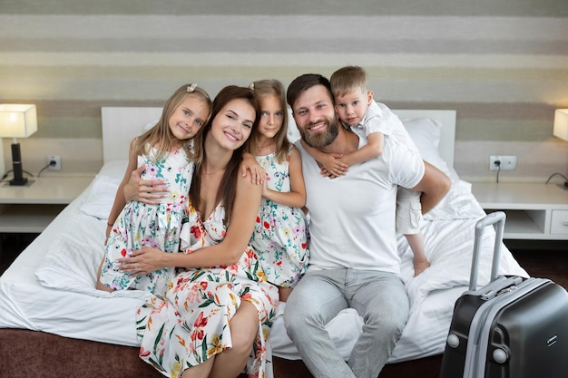 Junge Familieneltern mit Kindern sitzen im Hotel auf dem Bett und lachen Reisen mit Kindern