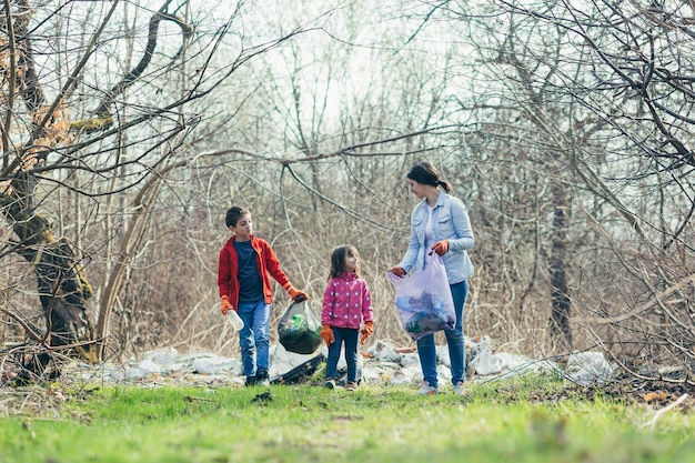 Junge Familienmutter mit zwei Kindern, die freiwillig den Frühlingspark reinigen, Müll und Plastikflaschen sammeln