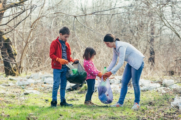 Junge Familienmutter mit zwei Kindern, die freiwillig den Frühlingspark reinigen, Müll und Plastikflaschen sammeln