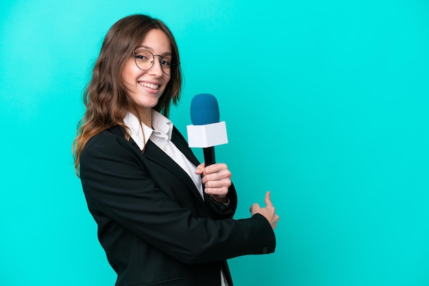 Junge Fernsehmoderatorin isoliert auf blauem Hintergrund, die nach hinten zeigt