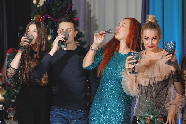 Junge festliche Frauen trinken Champagner in der Nähe des Weihnachtsbaums.