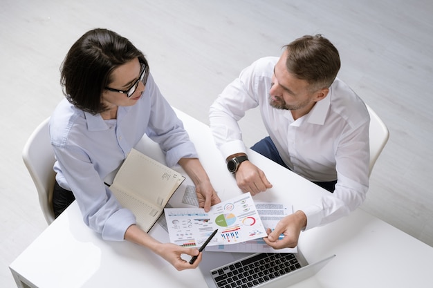 Junge Finanzierin und ihre Kollegin diskutieren Finanzpapiere beim Arbeitstreffen, während sie am Schreibtisch sitzen