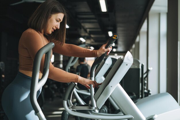 Foto junge fitness-brünette trainiert mit cardio-ausrüstung im fitnessstudio