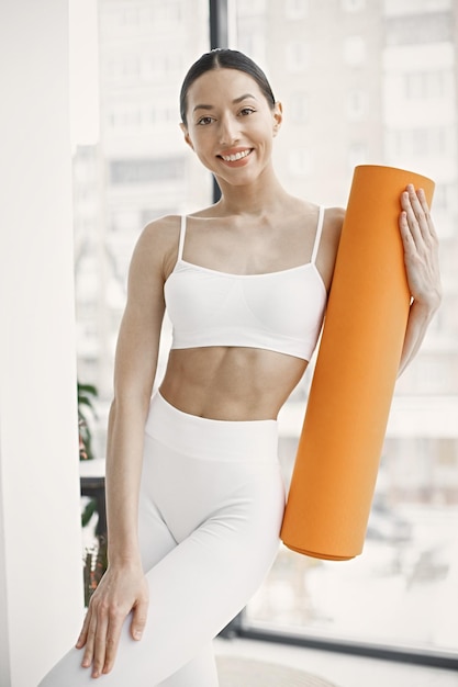 Junge Fitness-Frau bereit zum Training mit orangefarbener Yogamatte