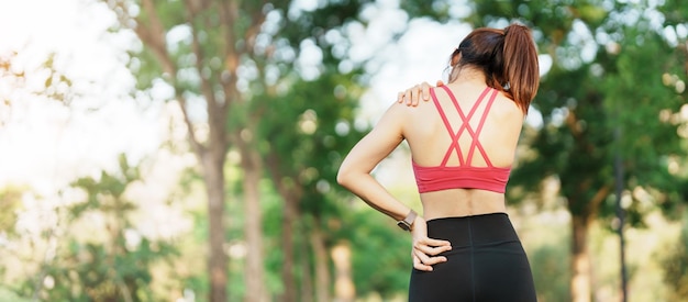 Junge Fitness-Frau, die ihre Sportverletzung Schulter- und Nackenmuskel während des Trainings schmerzhaft hält Asiatische Läuferin mit Körperproblemen nach dem Training im Freien im Sommer