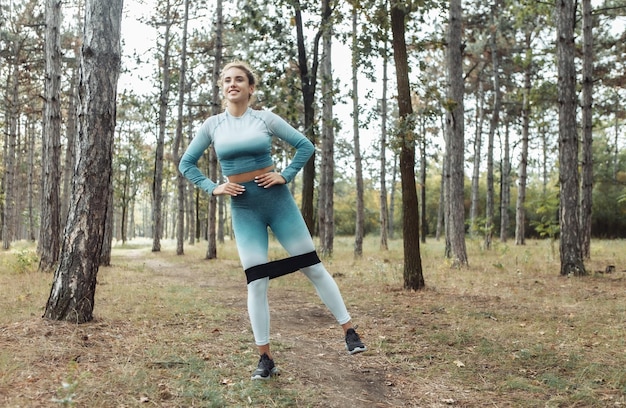 Junge Fitness-Frau mit lockigem Haar, die mit Fitness-Gummibändern im Wald trainiert