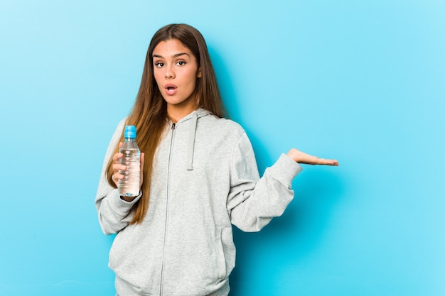 Junge Fitnessfrau, die eine Wasserflasche hält, beeindruckte das Halten des Kopienraums auf Handfläche.