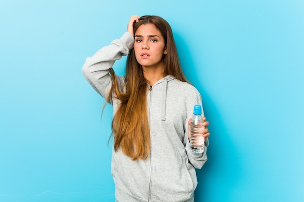 Junge Fitnessfrau, die eine Wasserflasche hält, die geschockt wird, sie hat sich an wichtiges Treffen erinnert.