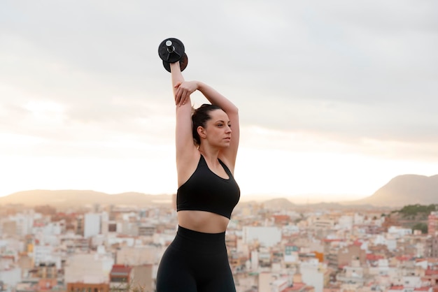 Junge Fitnessfrau hebt Gewichte im Freien bei Sonnenuntergang