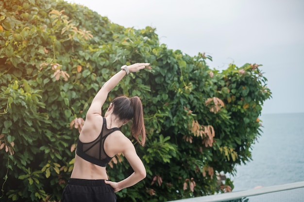 Junge Fitnessfrau in Sportkleidung, die Körper gegen Meerblick ausdehnt, gesunde Frauenübung am Morgen. Trainings-, Wellness- und Work-Life-Balance-Konzepte