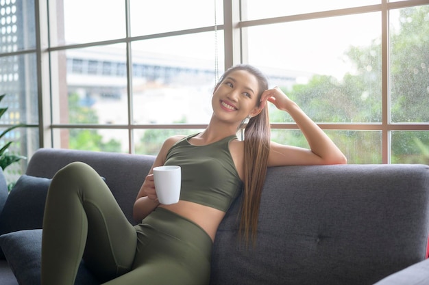 Junge Fitnessfrau in Sportkleidung, die nach dem Training zu Hause eine Tasse Kaffee trinkt