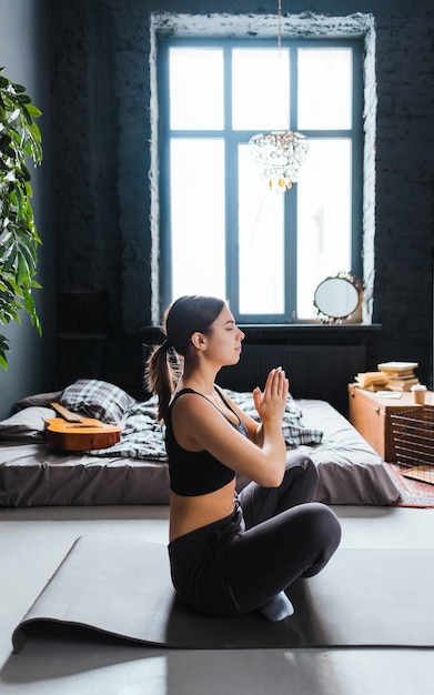 Junge Fitnessfrau meditieren, Yoga drinnen zu Hause in der Nähe des Bettes machend