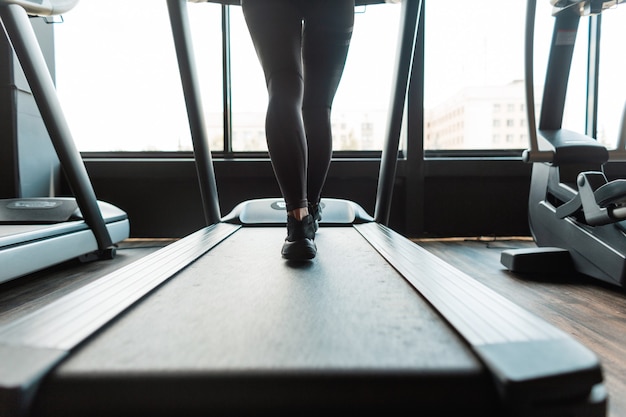 Junge Fitnessfrau mit Sportbekleidung und Turnschuhen läuft auf einem Laufband im Fitnessstudio