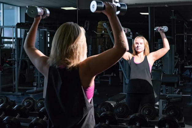 Junge fitte Frau an der Turnhalle, die schwere Übung mit Glocken macht. Sportlerin in einem Fitnessraum, der mit Hand wiegt