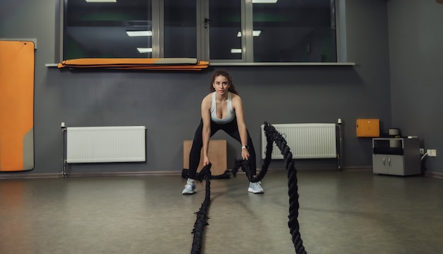 Junge fitte Frau, die Übung mit Kampfseilen in der Trainingsklasse tut. Funktionelles Training, Trainingsprozess.