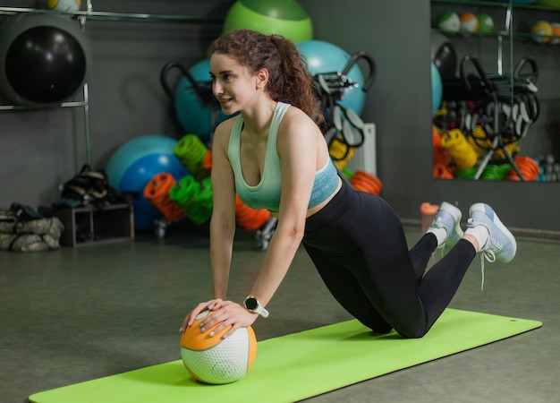 Junge fitte Frau, die Push-up-Übung mit Medizinball in der Sportklasse tut. Trainingsprozess