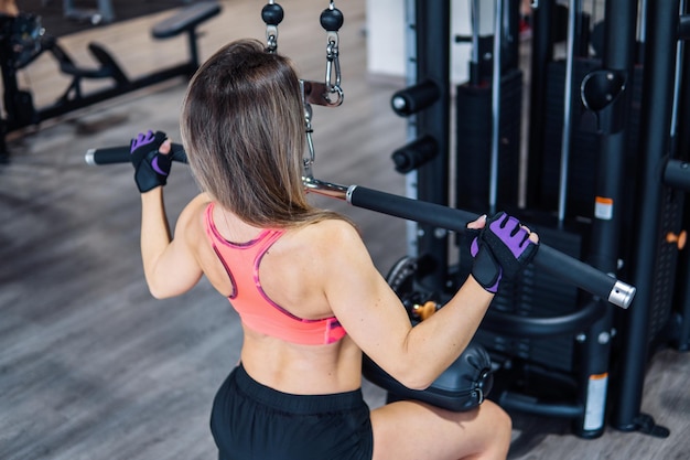 Junge fitte Frau, die Schulterübung mit Trainingsmaschine im Fitnessstudio macht. Ansicht von hinten.