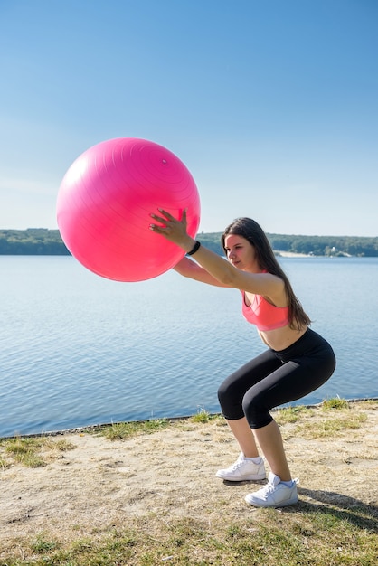 Junge fitte Frau in Sportkleidung während der Fitnesszeit und Training mit Ball am See. Gesunder Lebensstil