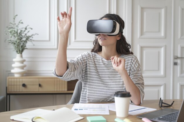 Junge fokussierte Frau mit Virtual-Reality-Headset, die sich bei der Arbeit Studieninhalte ansieht