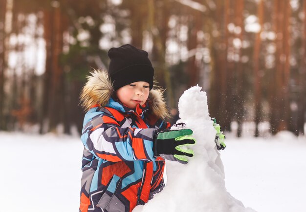 Junge formt Schneemann im Winter im Wald an einem sonnigen Tag