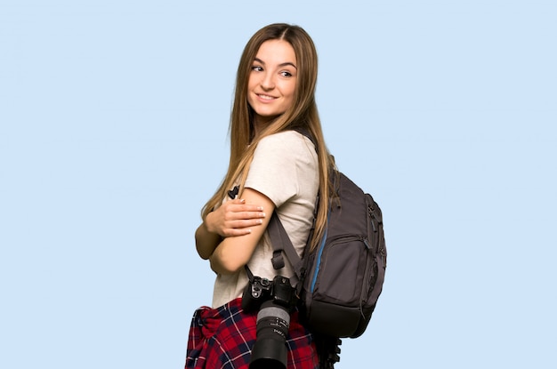 Junge Fotograffrau, die über der Schulter mit einem Lächeln auf lokalisiertem blauem Hintergrund schaut