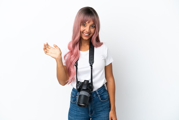 Junge Fotografin gemischtrassige Frau mit rosa Haaren isoliert auf weißem Hintergrund, die mit der Hand mit glücklichem Ausdruck grüßt