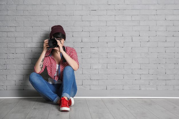 Junge Fotografin mit Kamera in der Nähe von Backsteinmauer