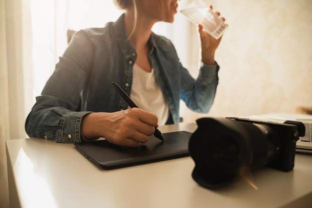 Junge Fotografin trinkt stilles Wasser an ihrem Arbeitsplatz