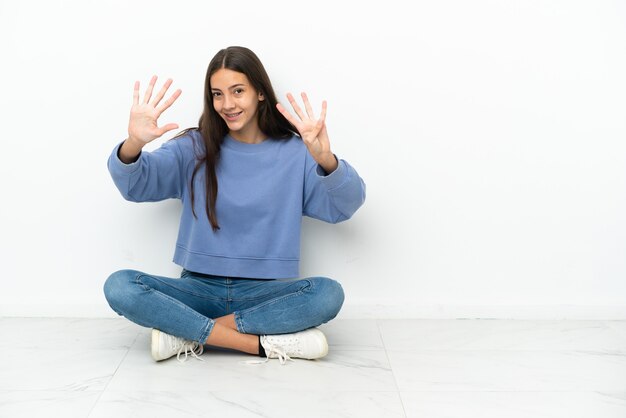 Junge Französin sitzt auf dem Boden und zählt neun mit den Fingern