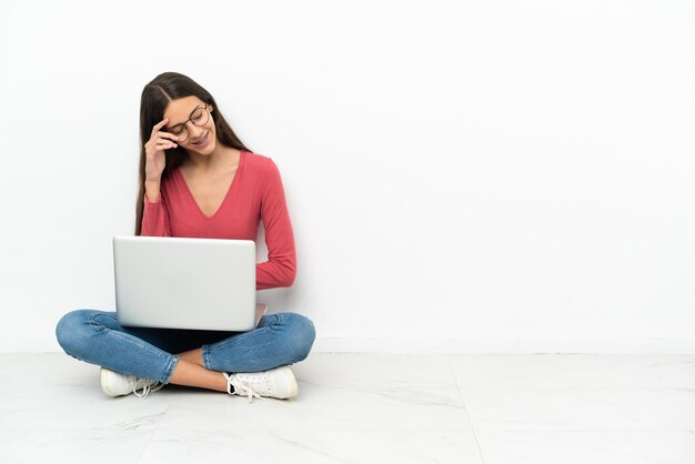 Junge Französin sitzt mit ihrem Laptop lachend auf dem Boden