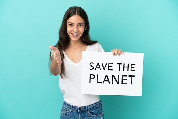 Junge französische Frau lokalisiert auf blauem Hintergrund, der ein Plakat mit Text Save the Planet hält, der einen Deal macht