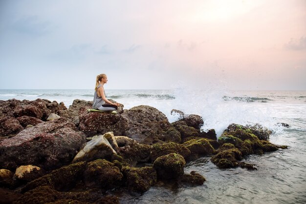 Junge Frau am Strand praktiziert Yoga an der Küste während des Sonnenuntergangs