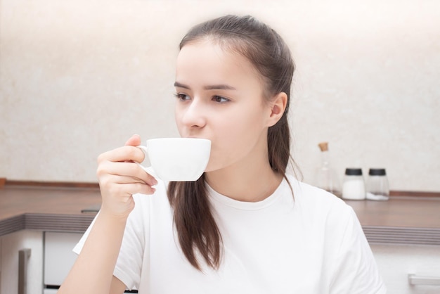 Junge Frau an einem Tisch in der Küche beim Frühstück trinkt Kaffee