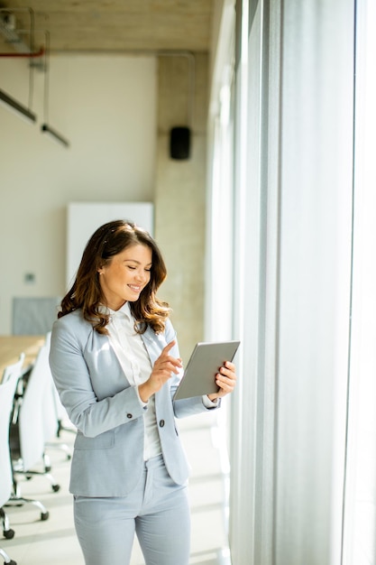 Junge Frau arbeitet am Bürofenster an einem digitalen Tablet