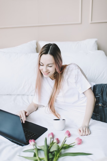 Junge Frau arbeitet am Laptop im Bett