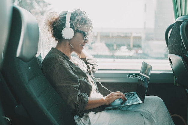 Junge Frau arbeitet am Laptop mit Headset, das auf dem Bussitz sitzt