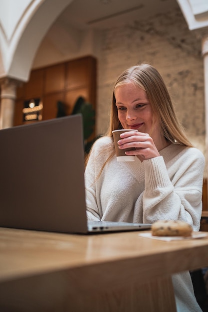 Junge Frau arbeitet hart mit ihrem Computer, während sie in einer Cafeteria einen Kaffee trinkt