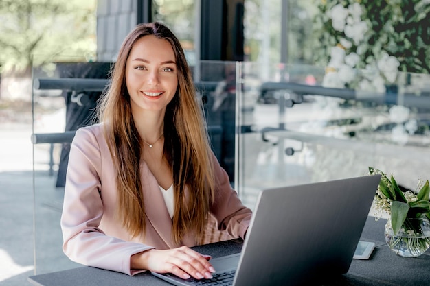 Junge Frau arbeitet lächelnd von einem Café aus mit Laptop