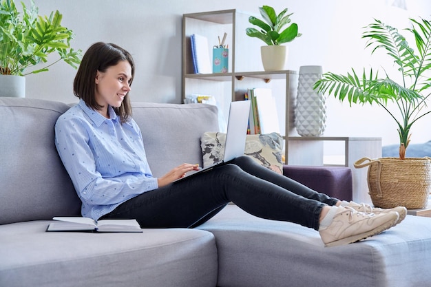 Junge Frau arbeitet von zu Hause aus mit Laptop und macht sich Notizen