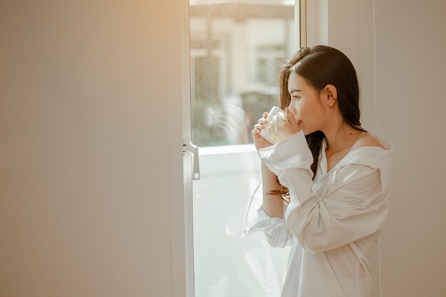 Junge Frau Asien wacht morgens erfrischt auf und isst im Urlaub entspannt Kaffee, Cornflakes, Brot und Apfel zum Frühstück im Haus. Asiatisch, Asien, Entspannen, Frühstück, Auffrischen, Lifestyle-Konzept.