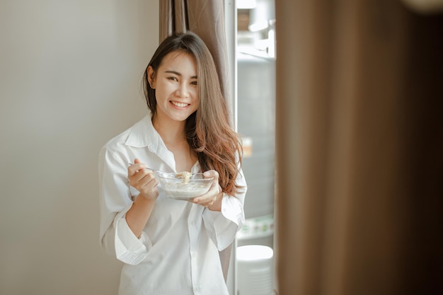 Junge Frau Asien wacht morgens erfrischt auf und isst im Urlaub entspannt Kaffee, Cornflakes, Brot und Apfel zum Frühstück im Haus. Asiatisch, Asien, Entspannen, Frühstück, Auffrischen, Lifestyle-Konzept.