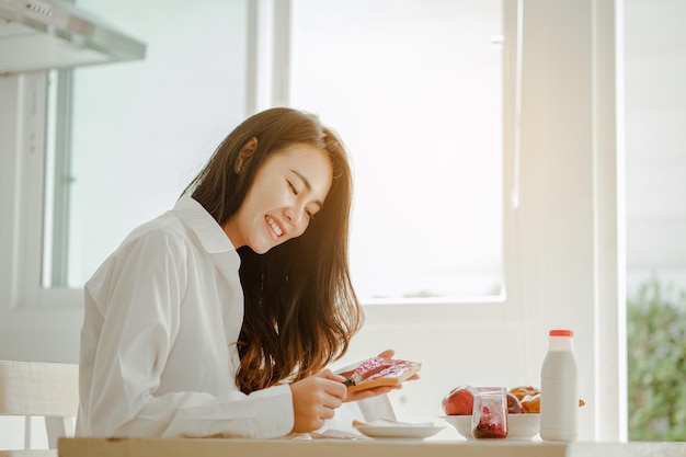 Junge Frau Asien wacht morgens erfrischt auf und isst im Urlaub entspannt Kaffee, Cornflakes, Brot und Apfel zum Frühstück im Haus. Asiatisch, Asien, Entspannen, Frühstück, Auffrischen, Lifestyle-Konzept.