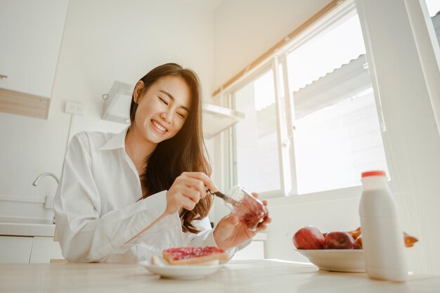 Junge Frau Asien wacht morgens erfrischt auf und isst im Urlaub entspannt Kaffee, Cornflakes, Brot und Apfel zum Frühstück im Haus. Asiatisch, Asien, Entspannen, Frühstück, Auffrischen, Lifestyle-Konzept.