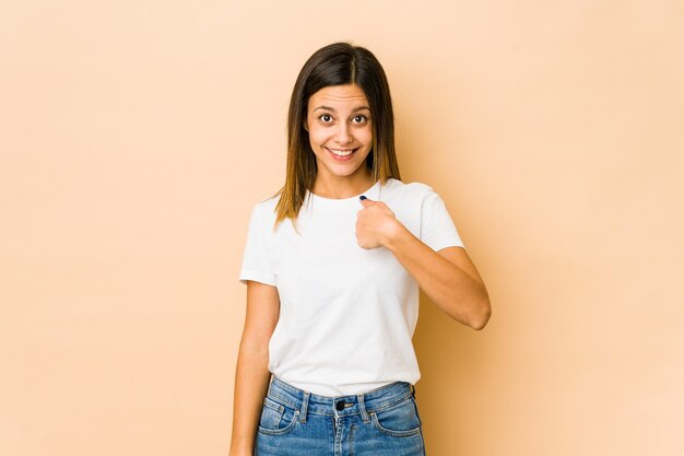 Junge Frau auf Beige überrascht, mit dem Finger zeigend, breit lächelnd.